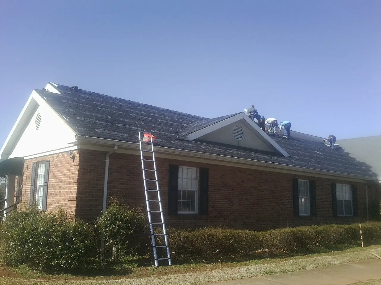 Crew tearing shingles off a brick ranch roof with a ladder set — Emergency Roof Repair work by our crew in Maxwell