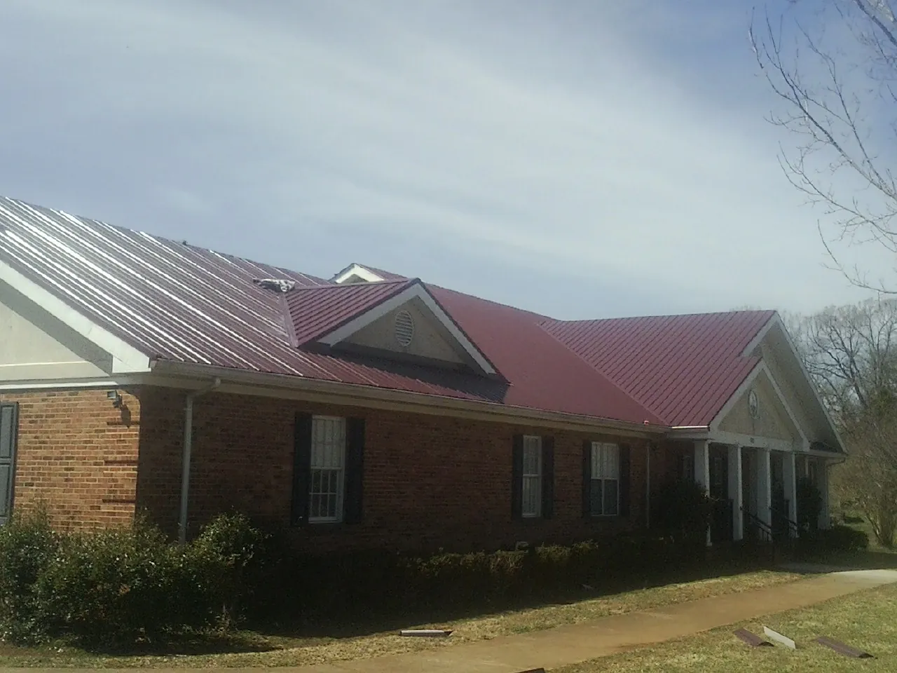 Red metal roof with gabled entries on a long brick building, from a Hail Damage Roof Repair job in Maxwell